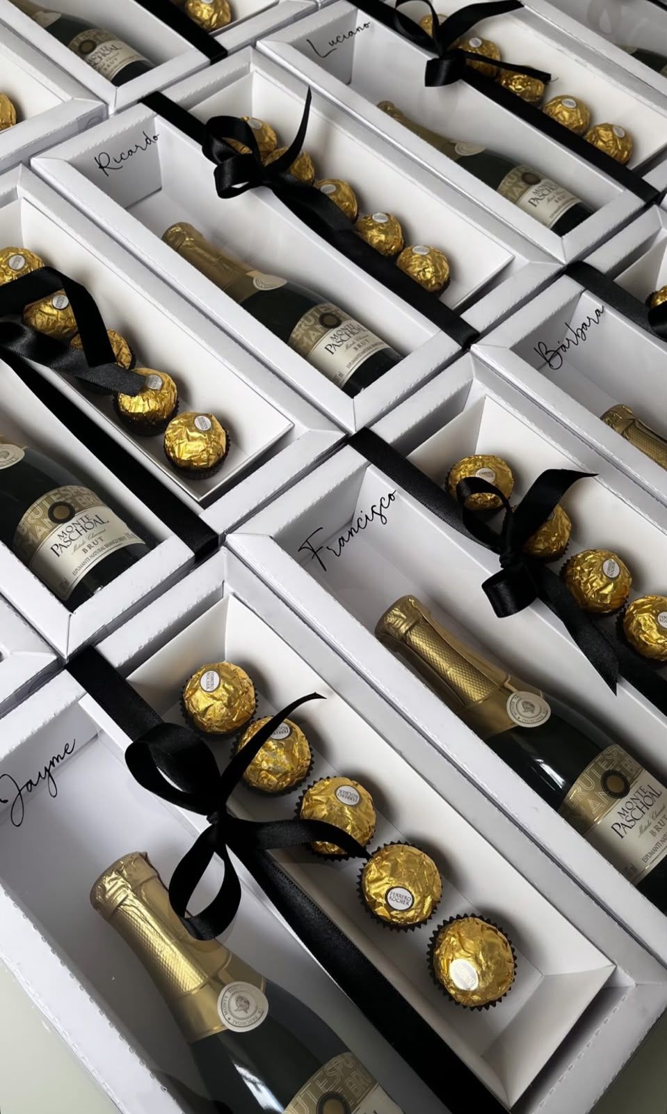 Caixas brancas com espumante, bombons e o nome de cada presenteado