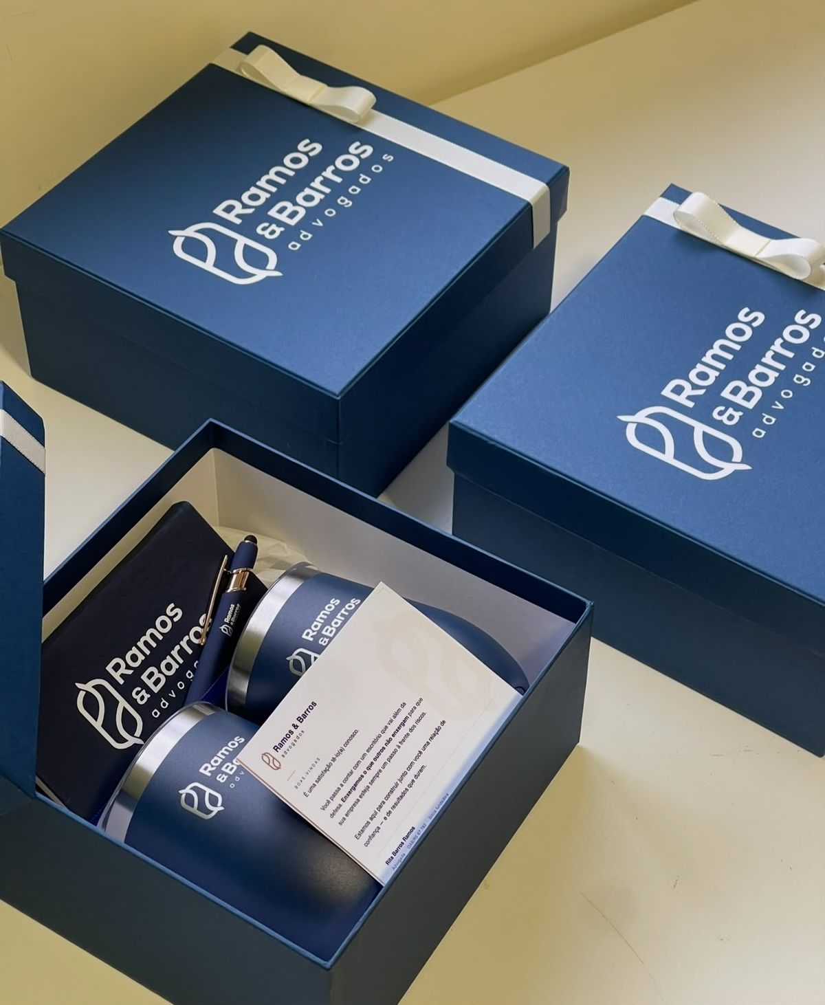 Caixas azuis com logo de escritório de advocacia, copos térmicos e caderno